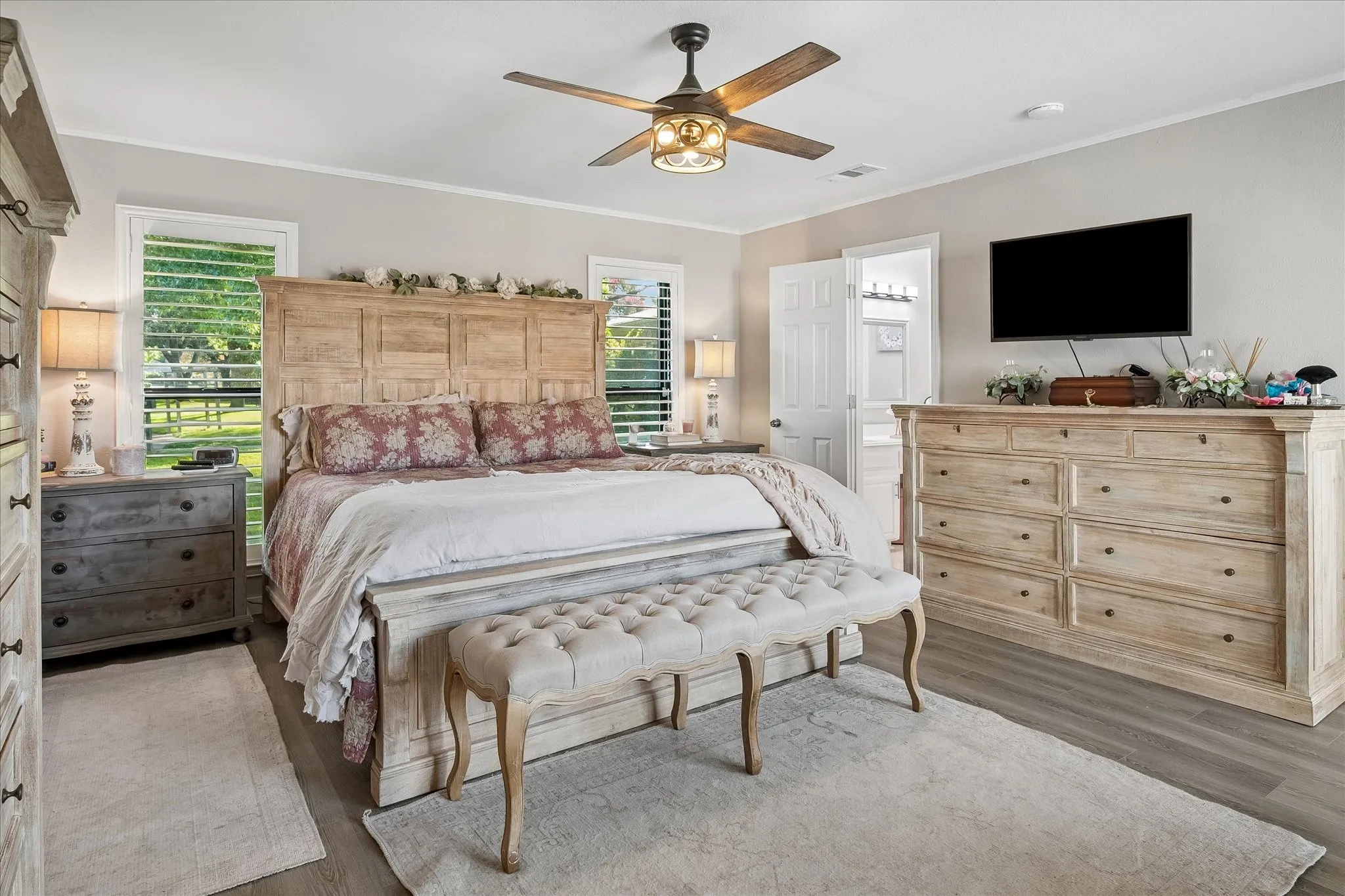 Bedroom featuring wood-finish flooring, a multi-blade ceiling fan with integrated lighting, dual windows with plantation shutters, and six-panel interior doors