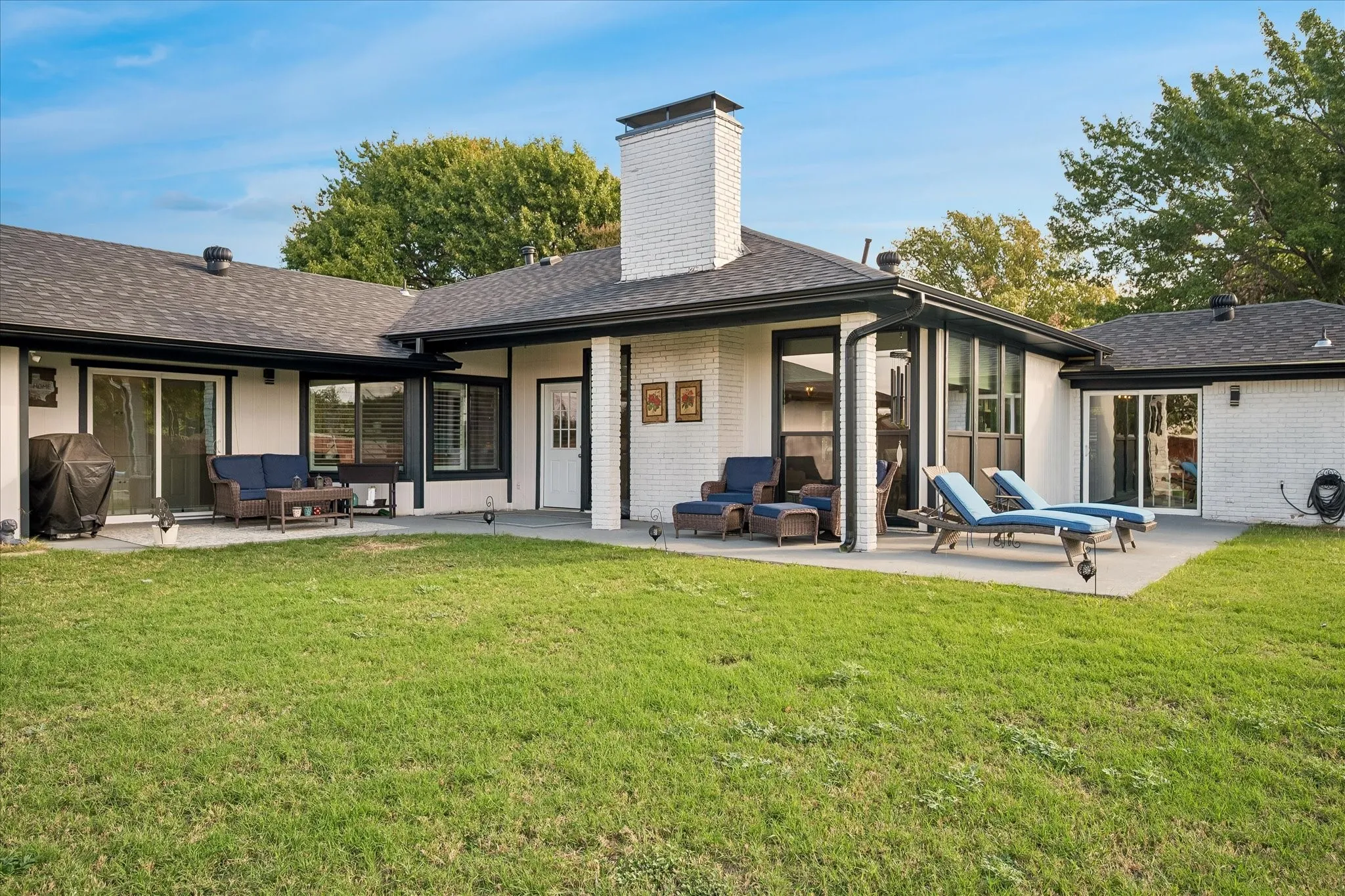 Painted brick exterior featuring a central chimney, concrete patio, multi-pane windows, and sliding glass entry points