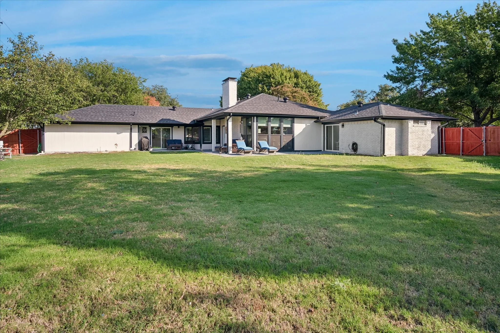 Expansive backyard featuring a manicured lawn, masonry chimney, covered patio, and perimeter wood fencing