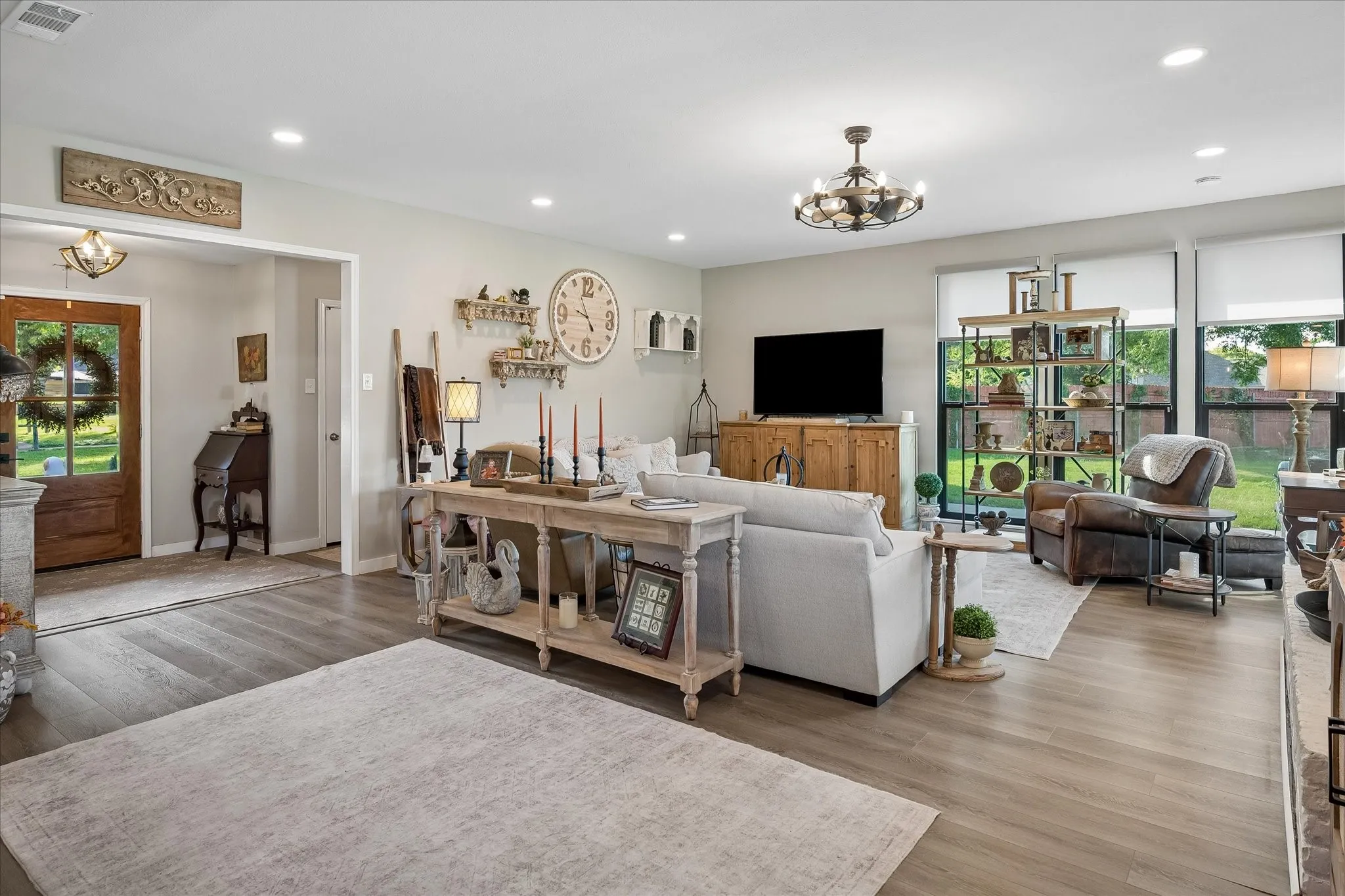 Open-concept living space featuring wood-finish flooring, recessed lighting, a multi-light chandelier, and large windows with integrated shades