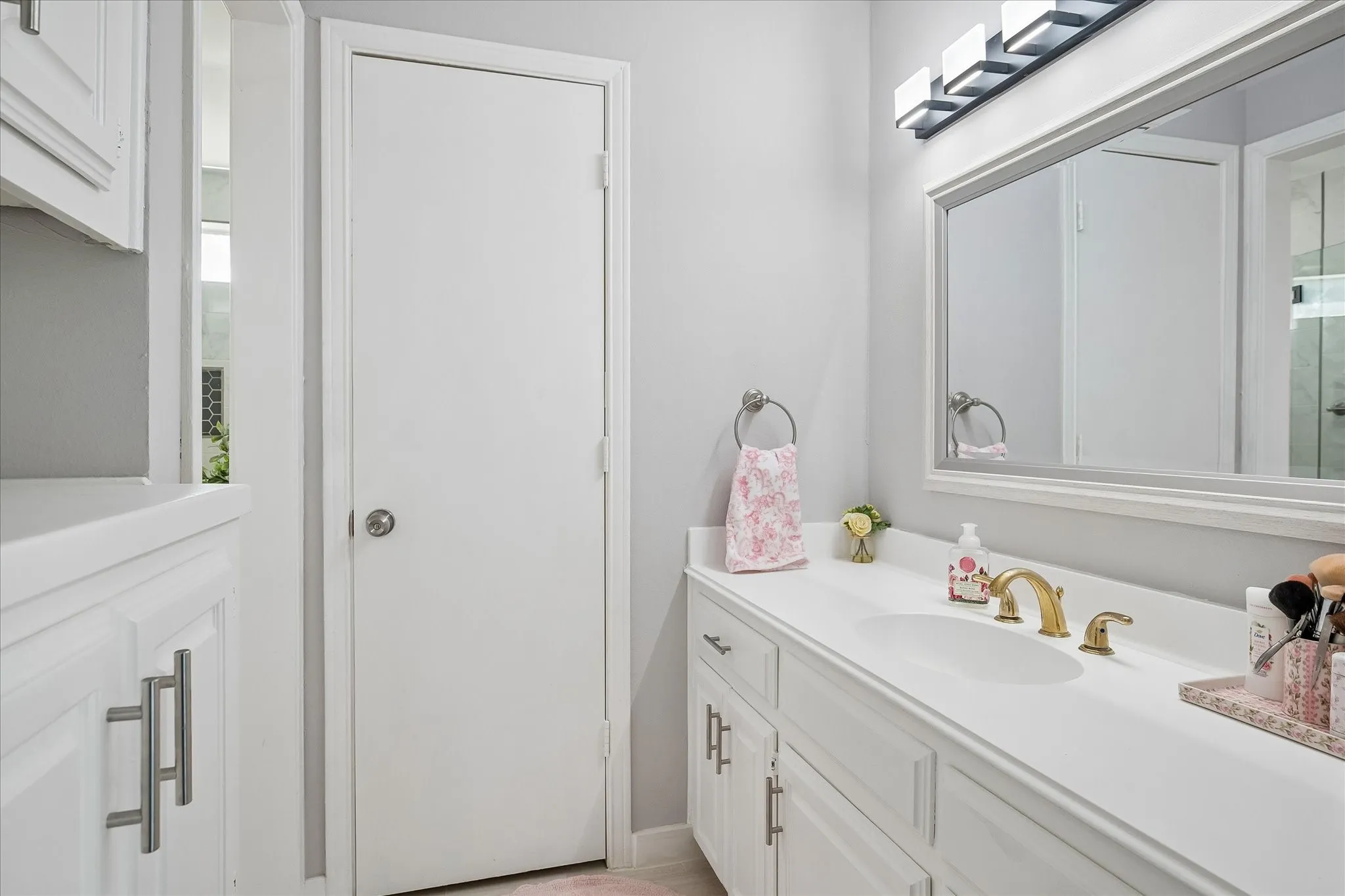 Bathroom vanity with white cabinetry, solid surface countertop, integrated sink, brass finish faucet, and rectangular wall-mounted mirror