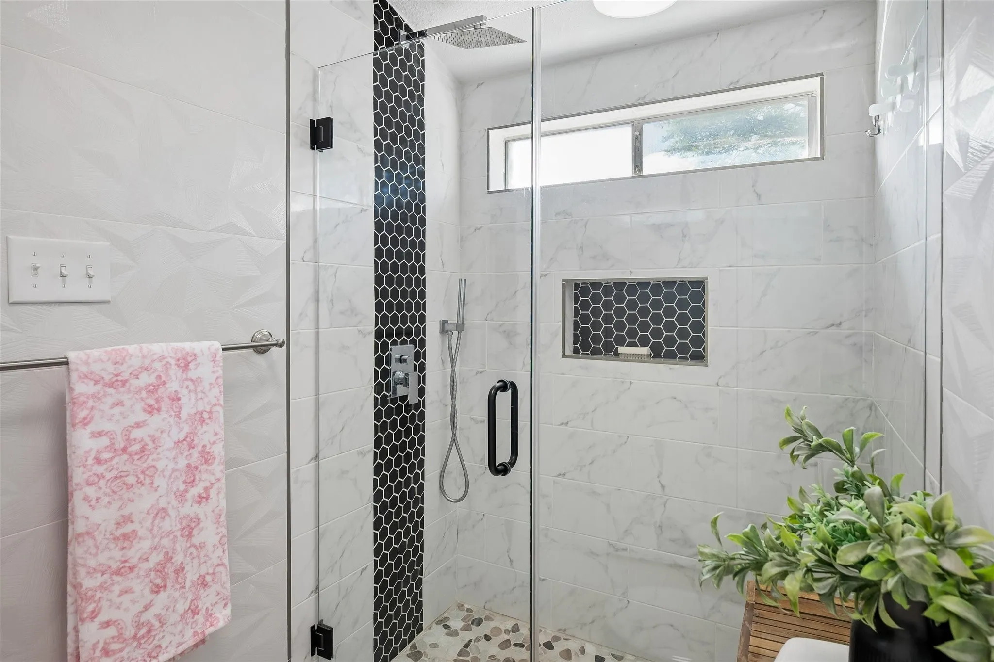 Walk-in shower featuring large-format white tile walls with textured geometric patterns, black hexagonal accent tiling, a built-in recessed niche, rainfall showerhead, and a clear glass enclosure