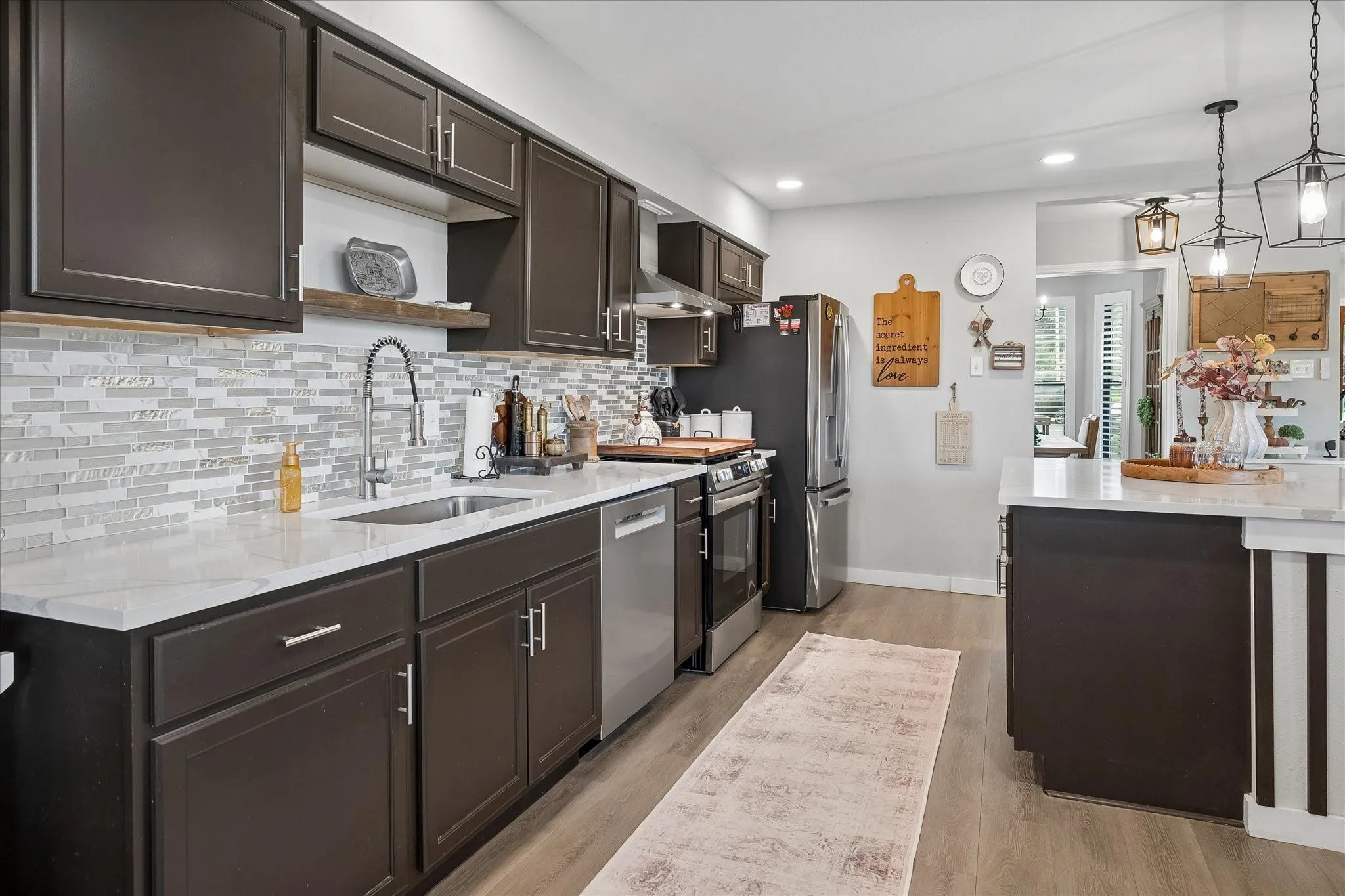 Kitchen featuring dark cabinetry, stone-style countertops, mosaic tile backsplash, wood-finish flooring, and pendant lighting