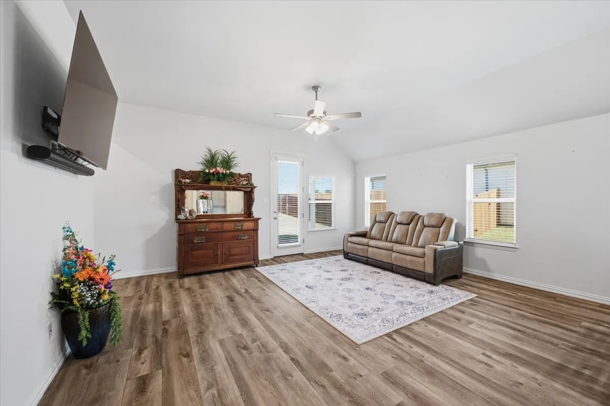 Spacious room featuring vaulted ceilings, wood-finish flooring, a ceiling fan, and multiple windows