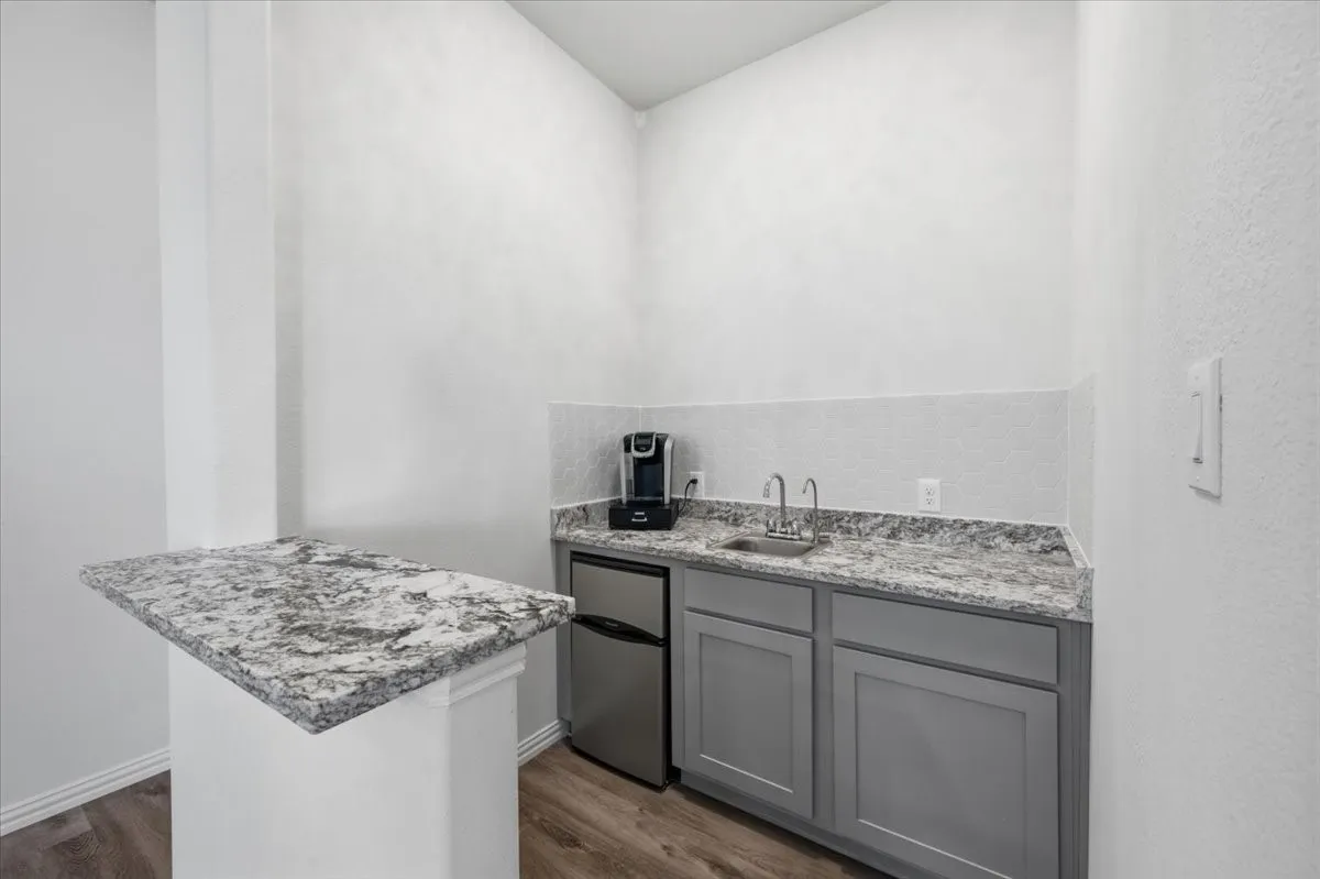 Wet bar with granite-style countertop, stainless steel sink, and gray cabinetry