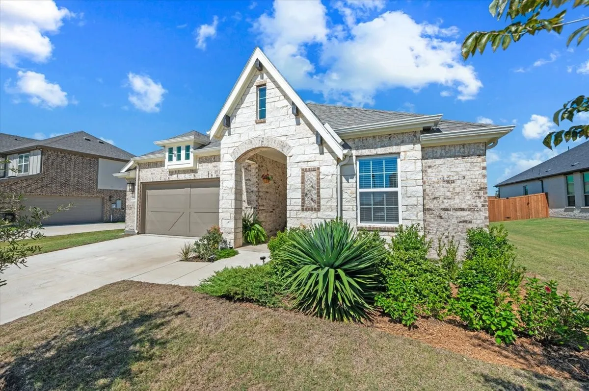 Stone and brick exterior with an arched entryway, two-car garage, and established landscaping
