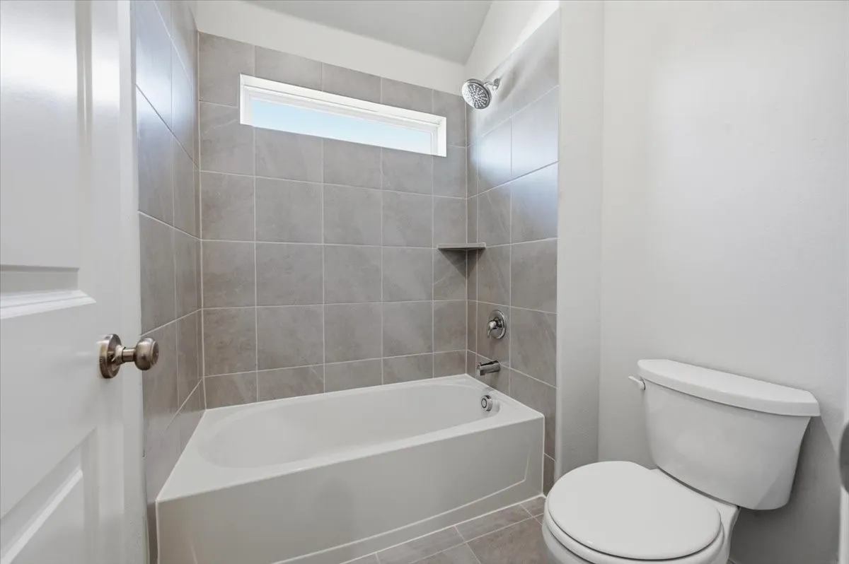 Bathroom with a white tub, shower with a tiled surround, a small privacy window, and a toilet