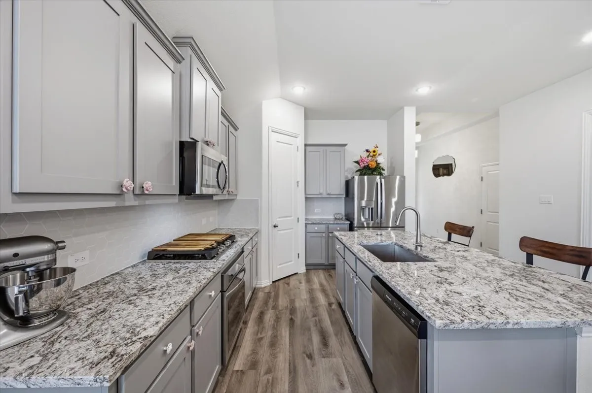 Kitchen featuring an extended island, light grey cabinetry, stainless steel appliances, wood-finish flooring, and recessed lighting
