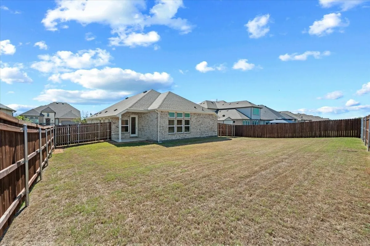 Expansive backyard with a full privacy fence, brick exterior, and covered patio