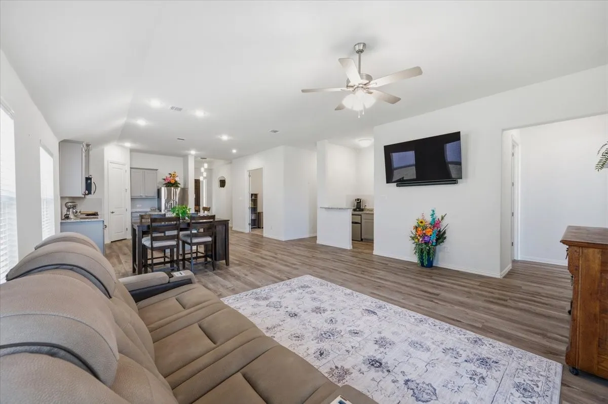 Wood-finish flooring throughout, white walls, and a ceiling fan with integrated lighting