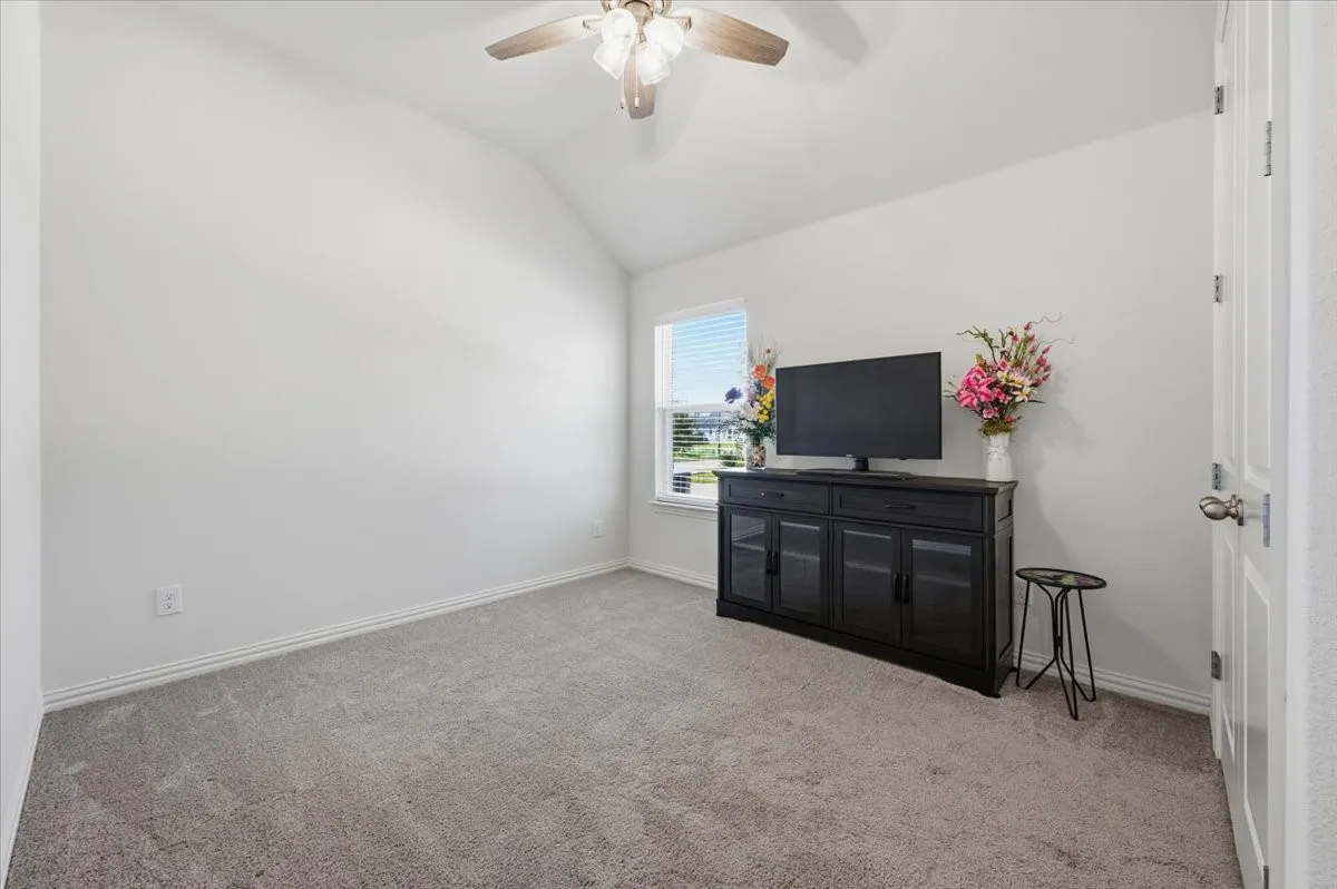 Vaulted ceiling with a ceiling fan, light gray carpeting, and a window with blinds