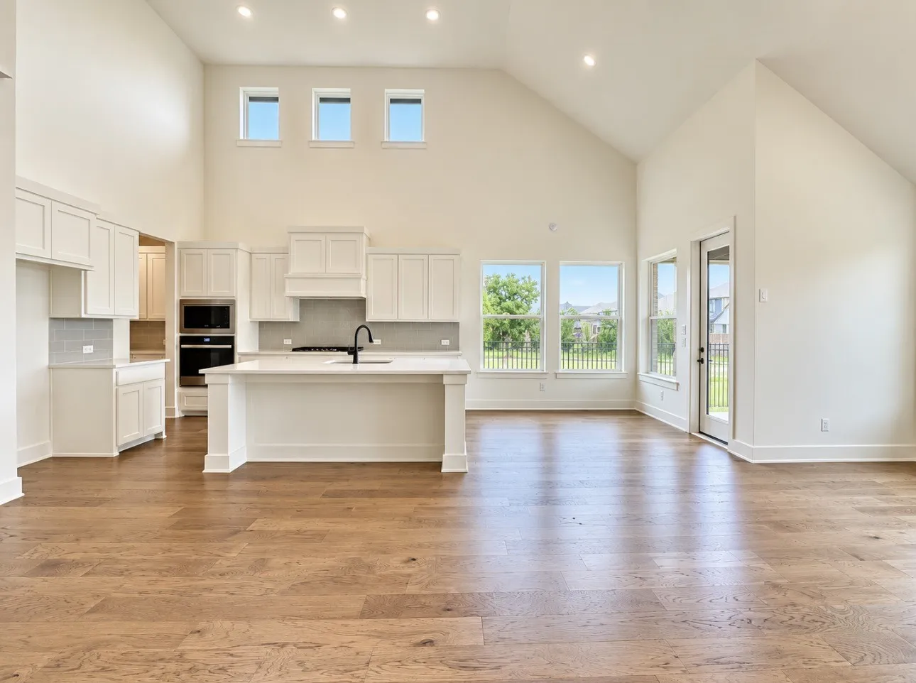 Vaulted ceiling with recessed lighting, wood-finish flooring, white cabinetry, integrated stainless steel appliances, and a central island with a sink