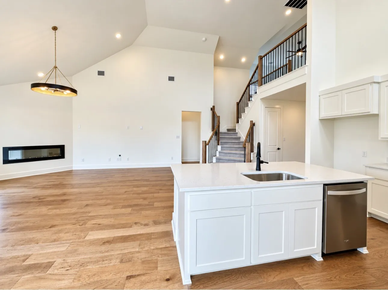 Open-concept living space featuring vaulted ceilings, wood-finish flooring, a modern linear fireplace, and a kitchen island with an integrated sink