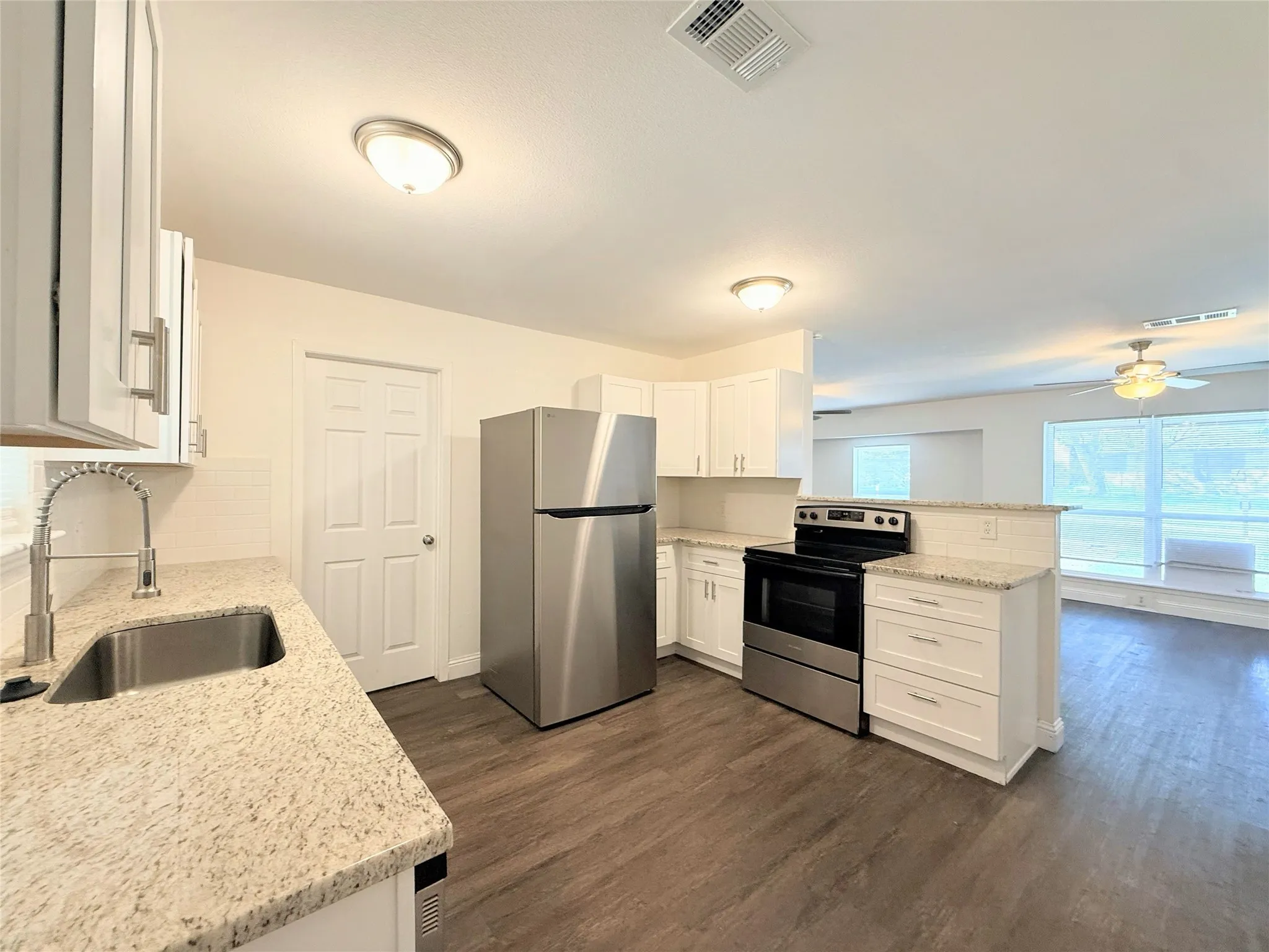 Kitchen featuring white cabinetry, granite countertops, stainless steel appliances, and wood-finish flooring