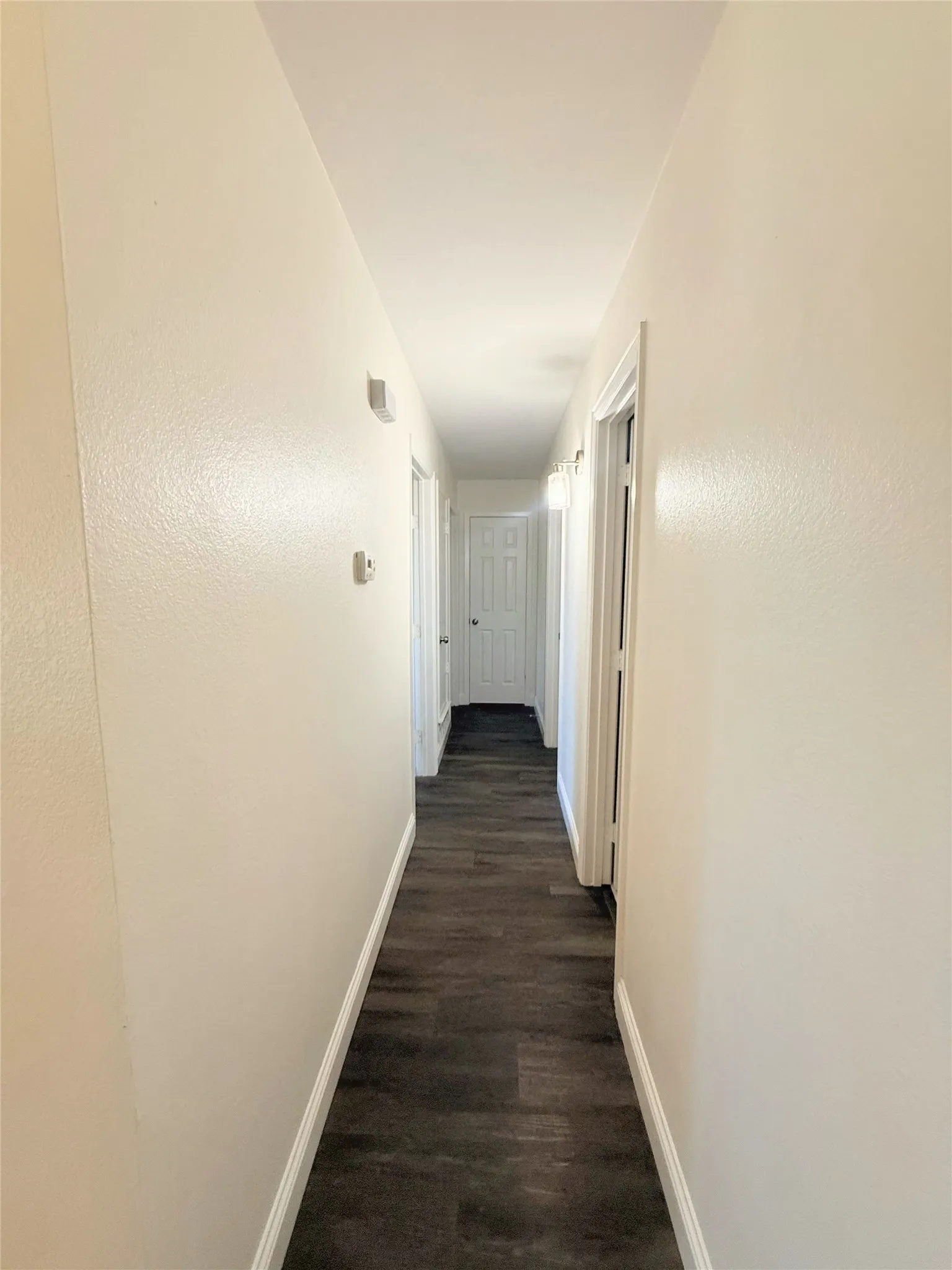 Hallway with wood-finish flooring, white walls, and white trim
