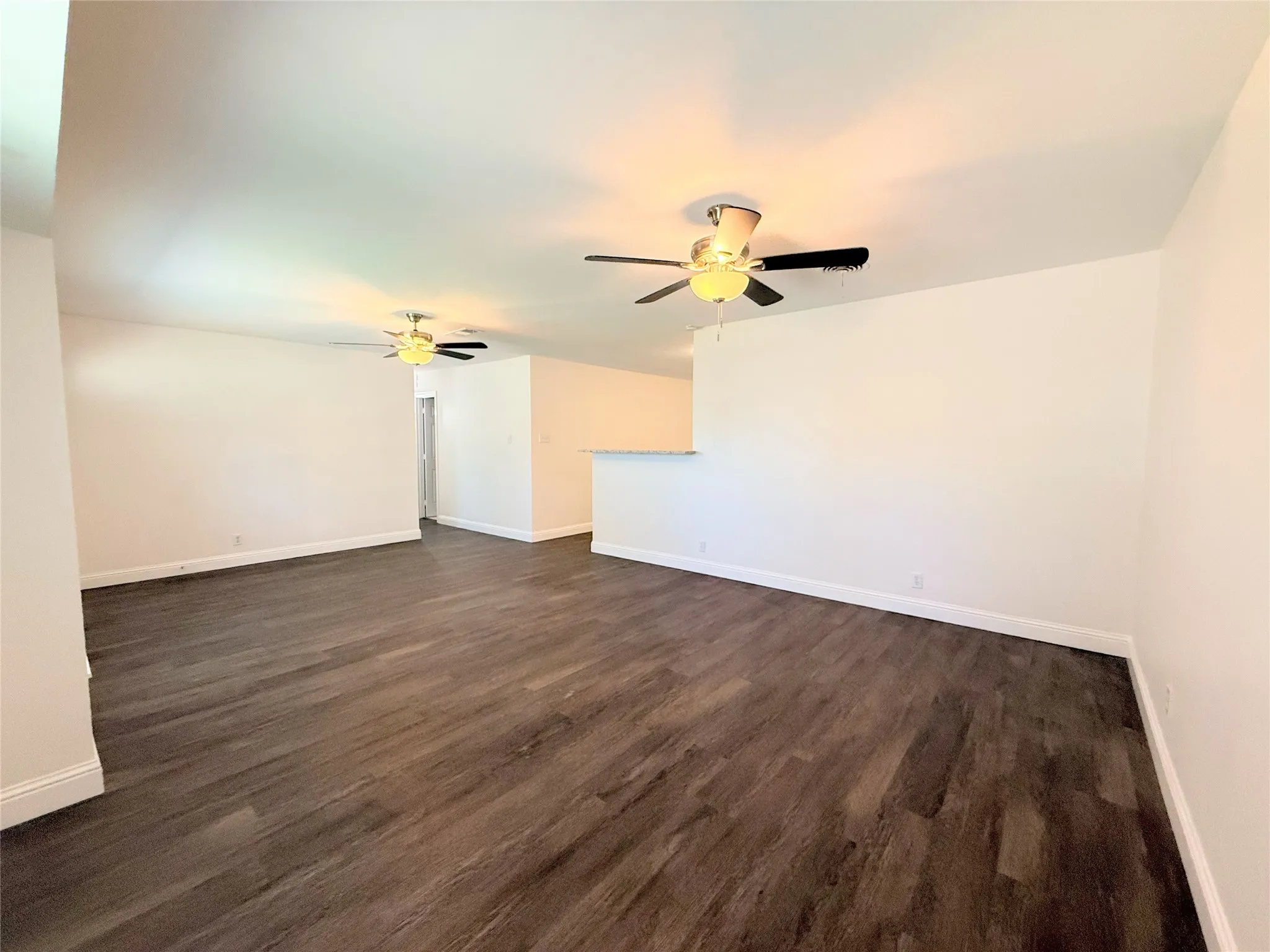 Wood-finish flooring throughout, paired with a half wall feature and ceiling fans