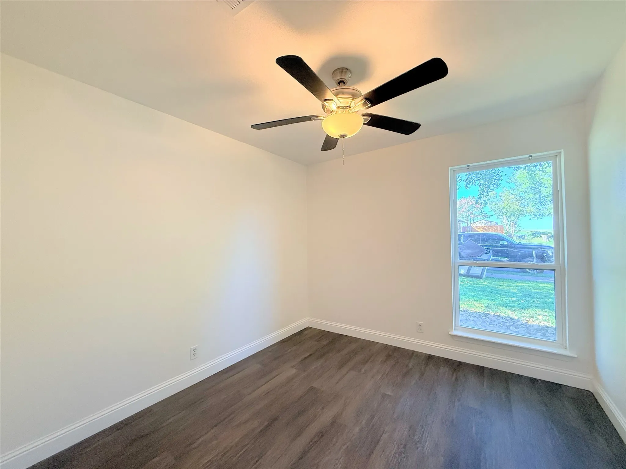 Bright corner bedroom with wood-finish flooring, ceiling fan with integrated lighting, and large window with natural light exposure