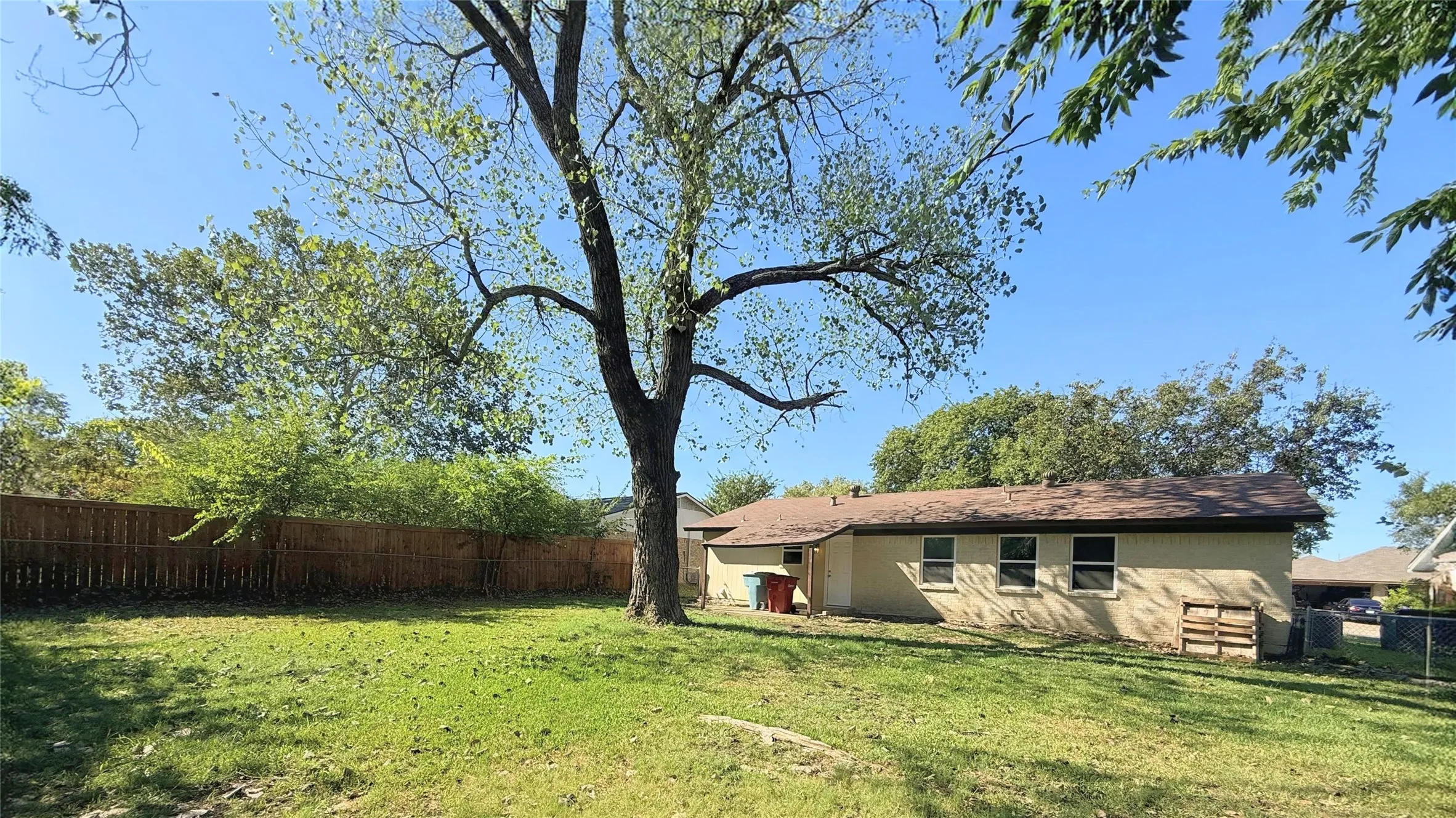 Spacious residential property situated on expansive grounds featuring mature shade trees, open lawn area, and a single-story brick structure with attached outbuildings