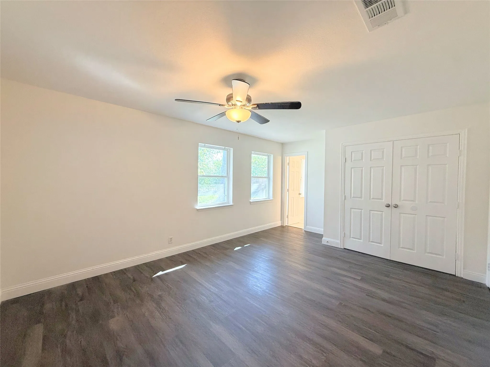 Wood-finish flooring, dual windows, ceiling fan with integrated lighting, and white bi-fold closet doors