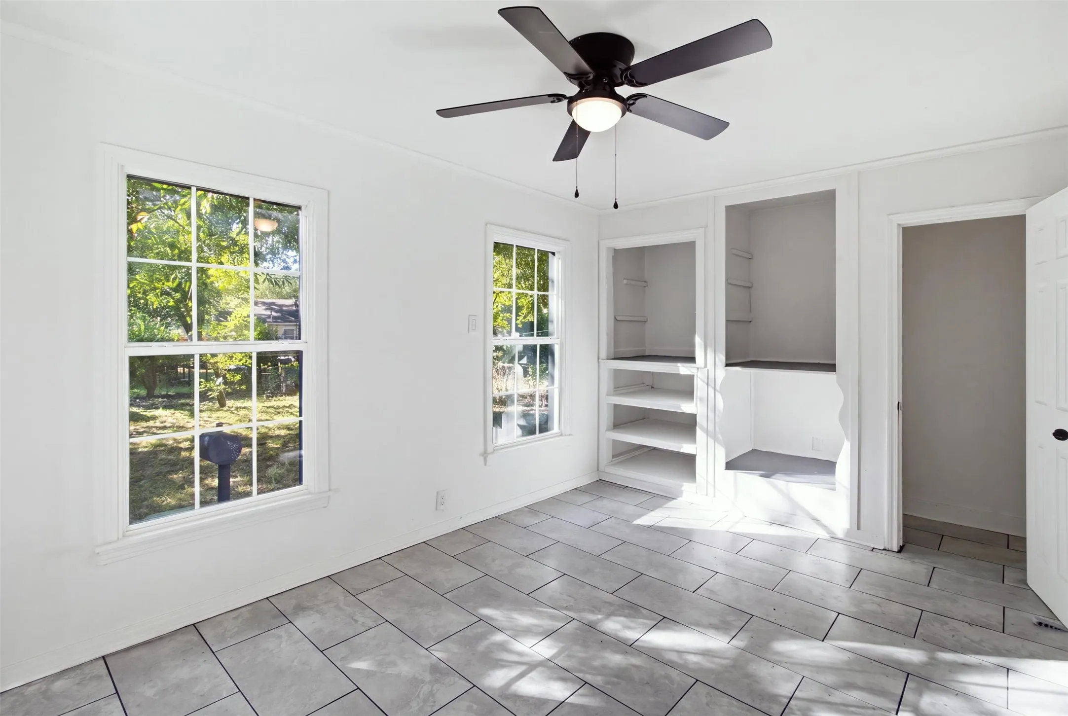 Bright, light-filled room featuring tile flooring, multiple windows with natural light, ceiling fan with pull-chain controls, and direct access to adjacent spaces through French doors with integrated blinds