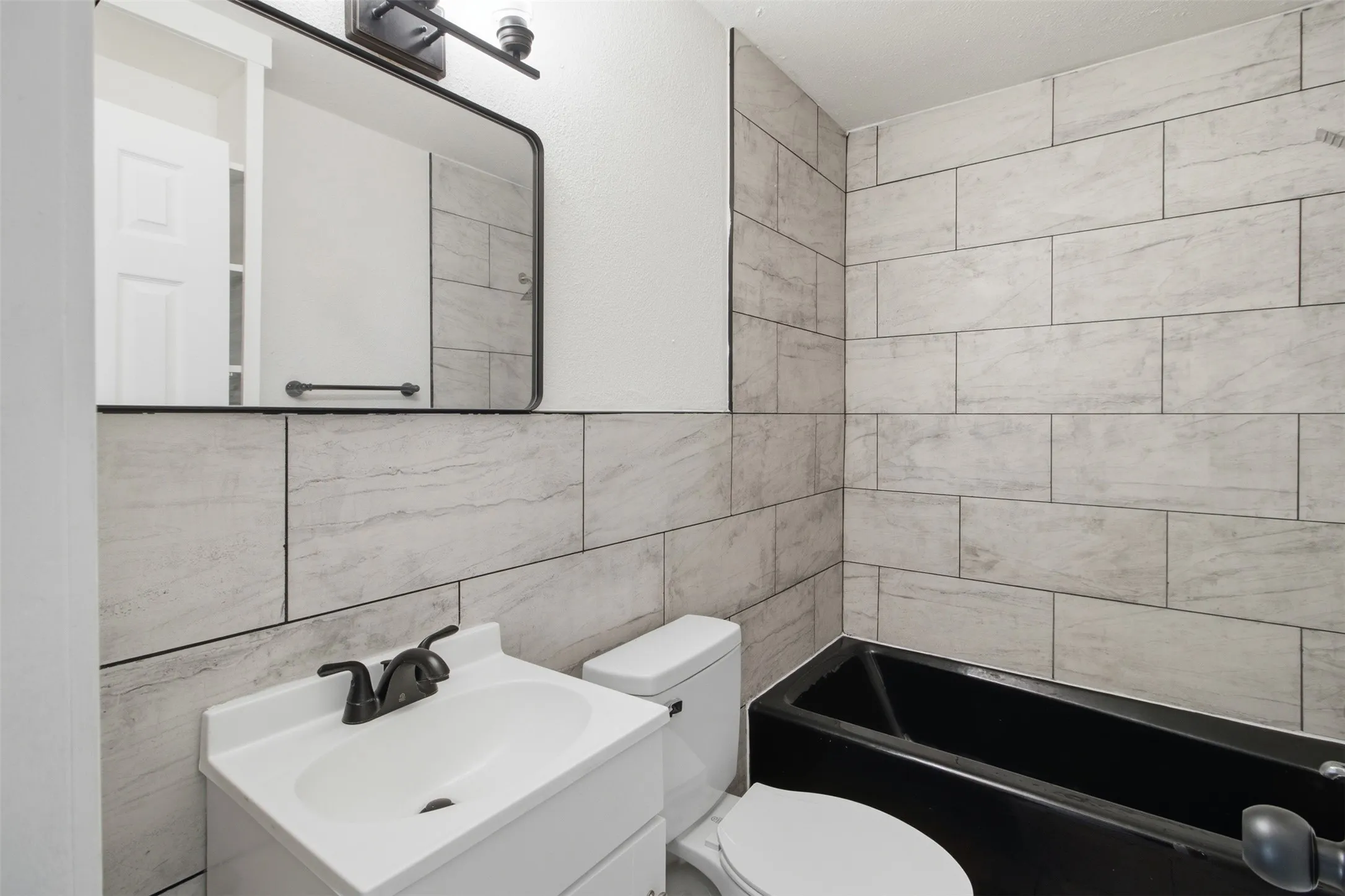Bathroom featuring a black bathtub, white vanity with integrated sink, and light-toned rectangular wall tiling