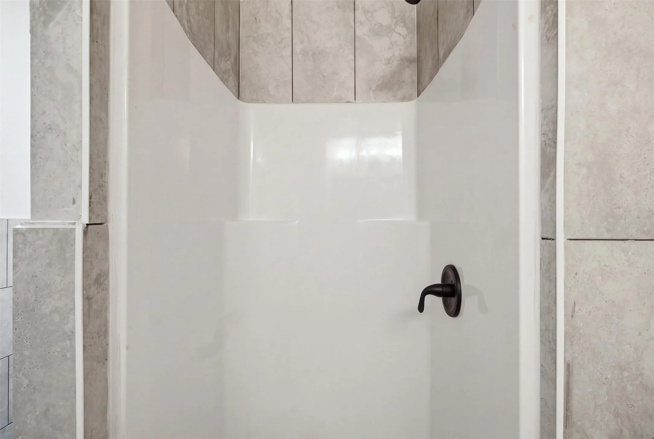 White shower stall with a single-handle matte black faucet and light-toned tile surround