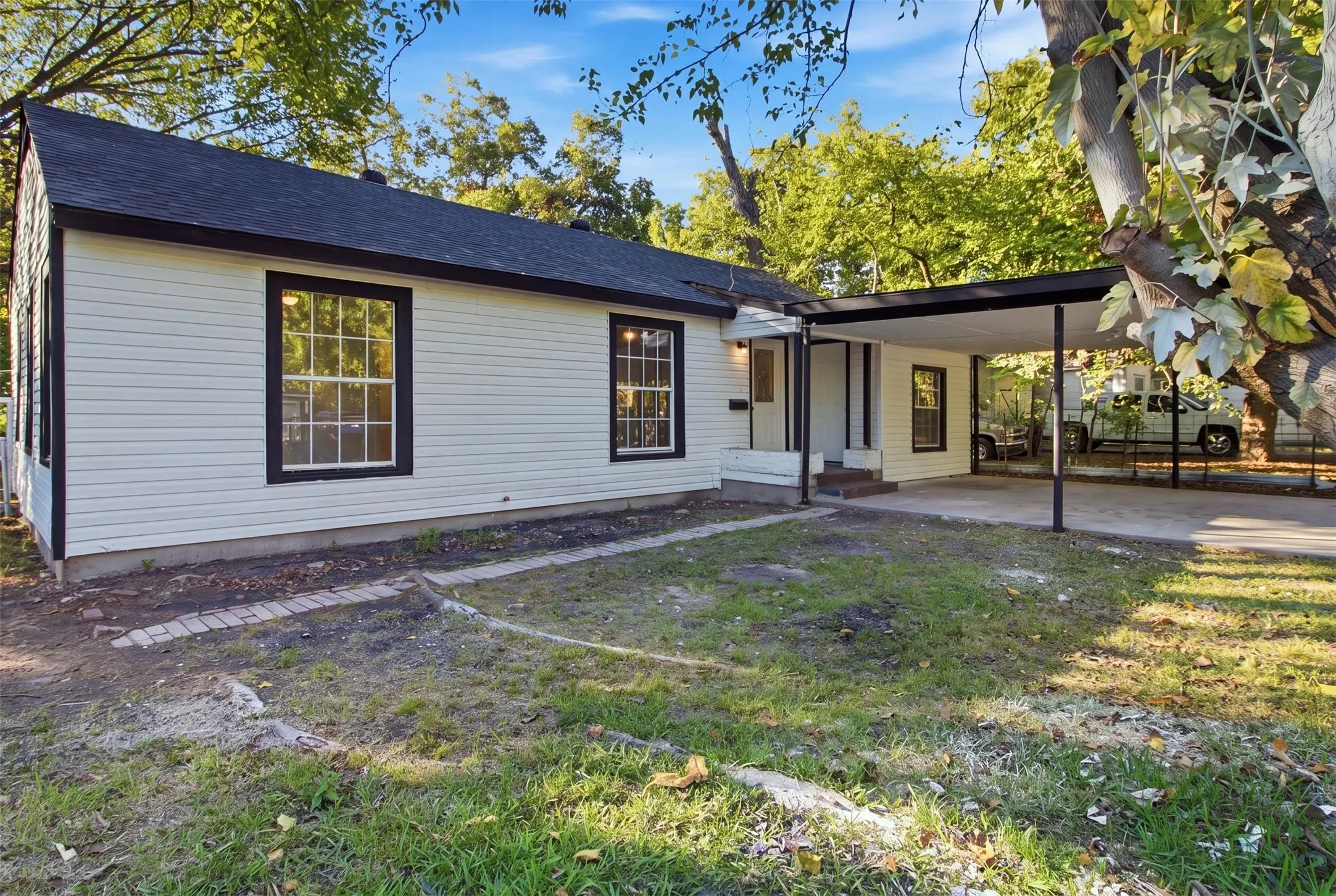 White horizontal siding exterior with black trim windows, a dark roof, and a covered carport