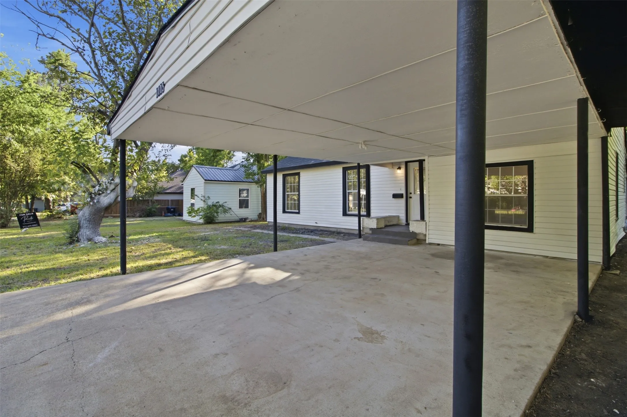 Carport with concrete pad, white siding exterior, and black trim windows