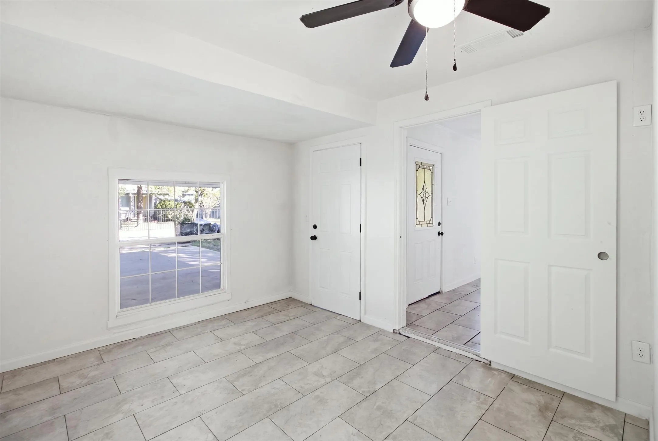 Tile flooring, ceiling fan, white paneled doors, window with grid, and a door with decorative glass