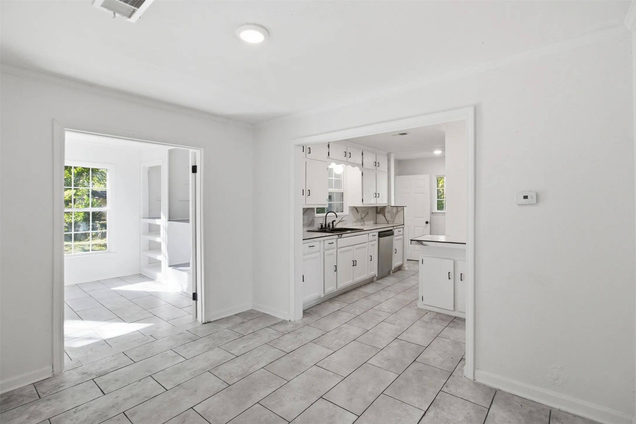 White kitchen cabinetry, stainless steel dishwasher, and tiled flooring