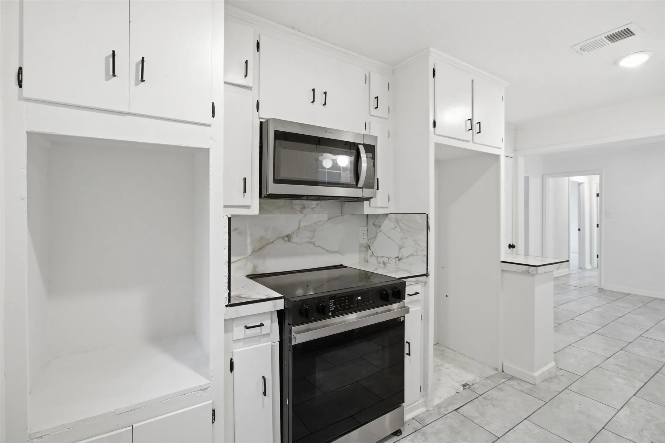 White cabinetry with black hardware, stainless steel microwave, black electric range, marble-patterned backsplash, and tile flooring