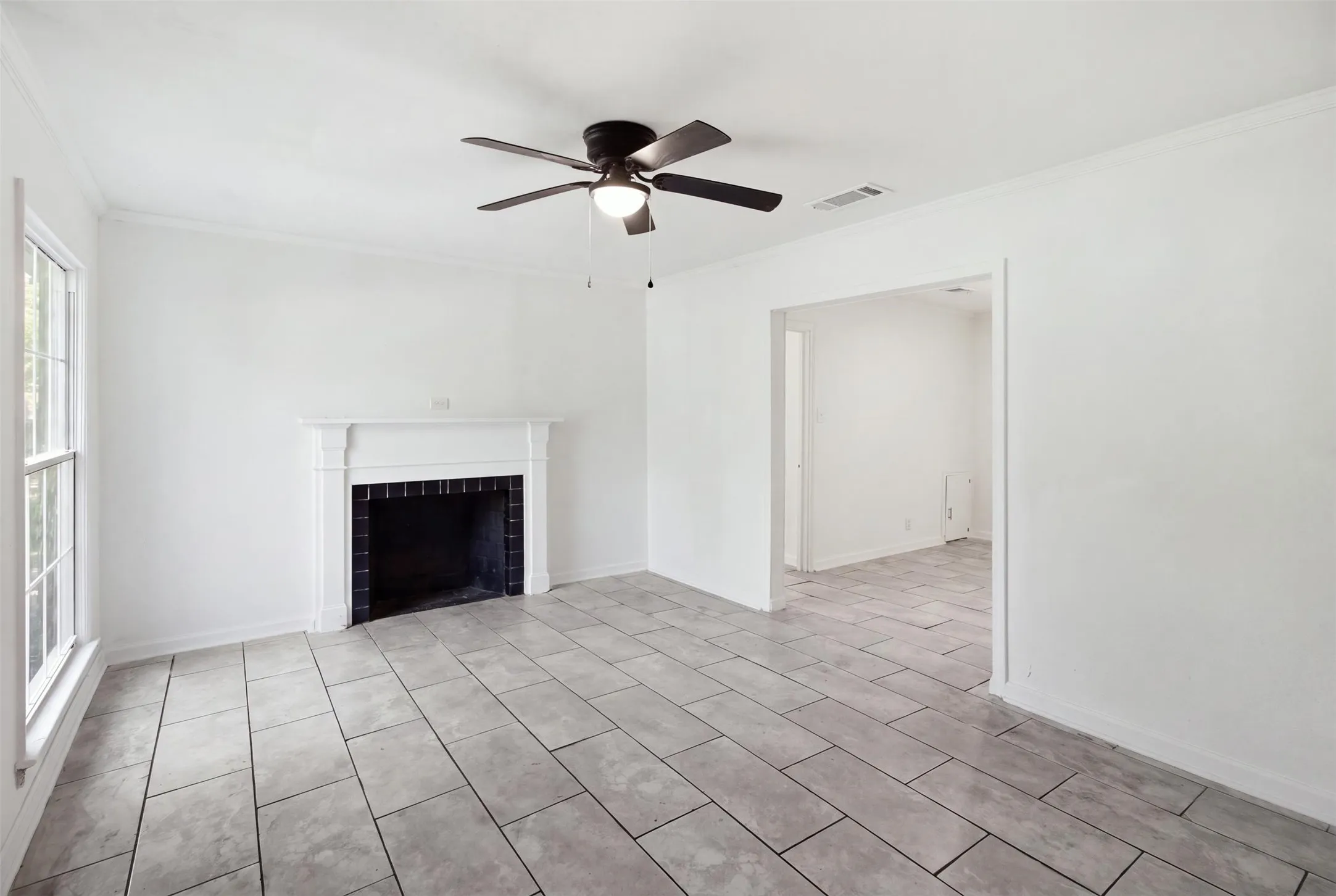 Spacious living area featuring diagonal tile flooring, a fireplace with black surround, ceiling fan with integrated lighting, and abundant natural light from large windows