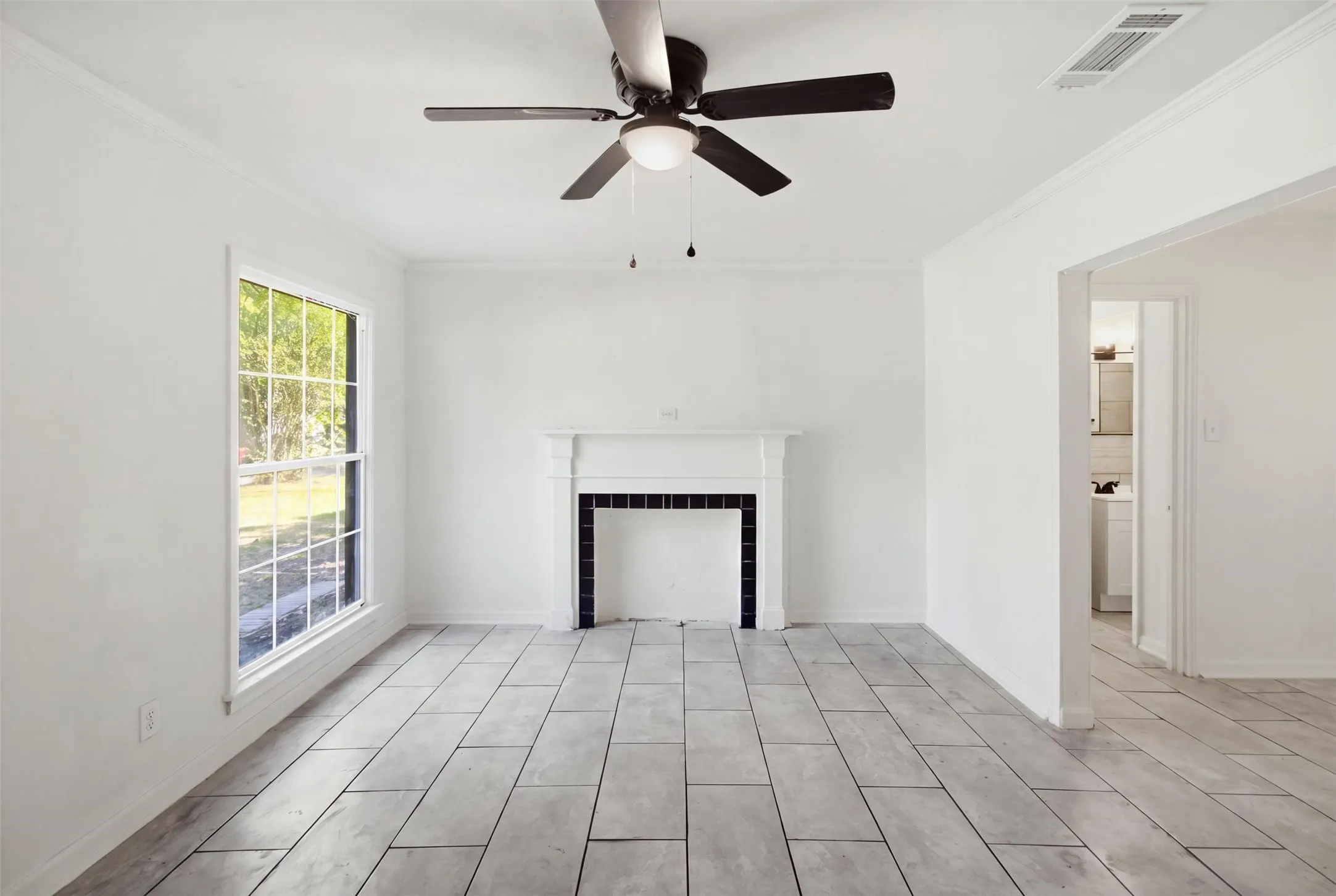 Expansive room with tile flooring, a decorative fireplace, a multi-pane window, and a ceiling fan with integrated lighting