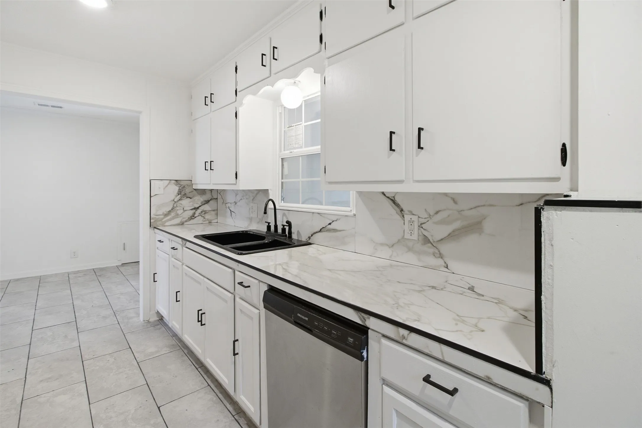 White cabinetry with black hardware, marble-patterned countertops and backsplash, stainless steel dishwasher, black sink with black faucet, and tiled flooring