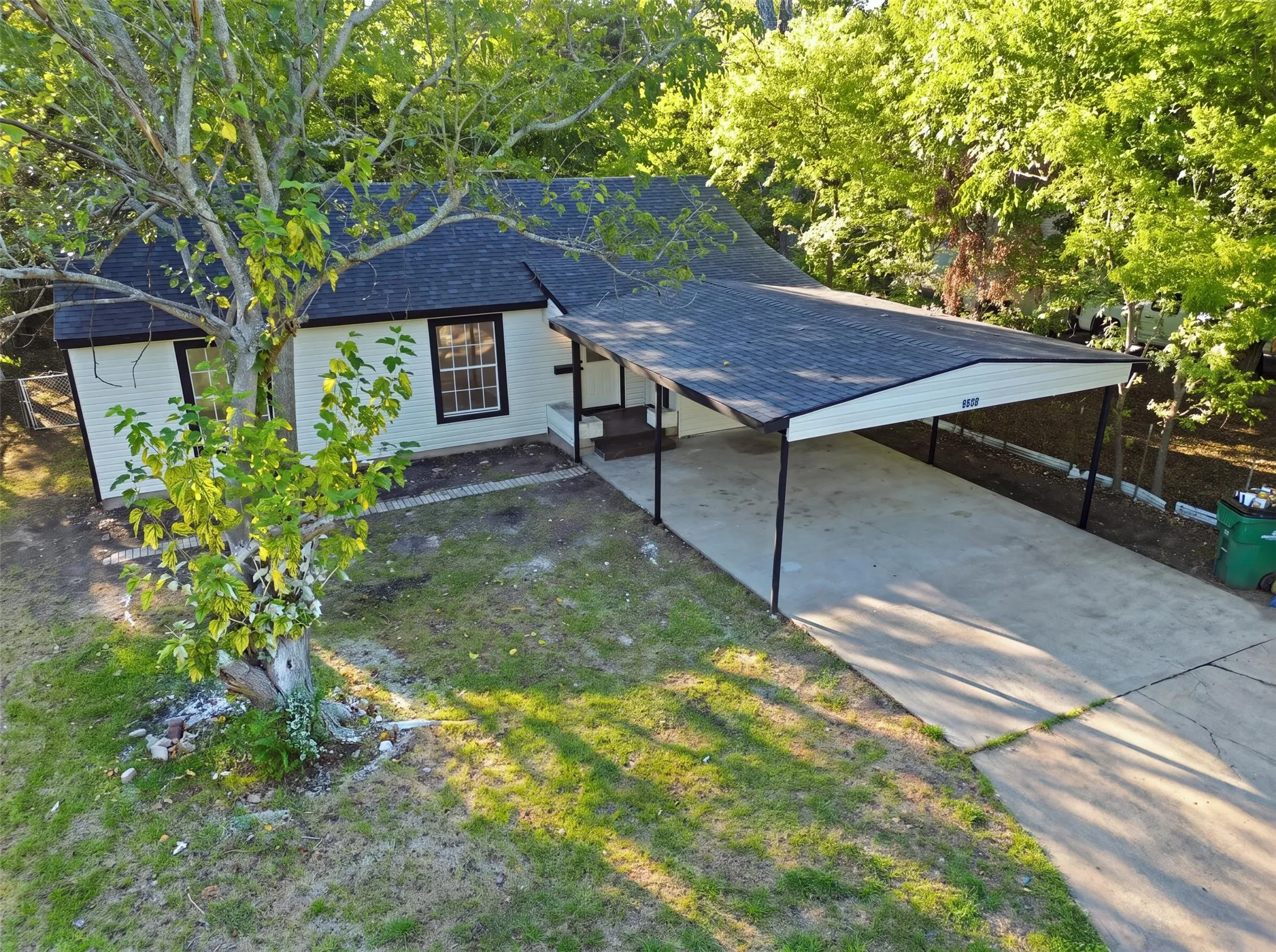 Exterior featuring white siding, dark trim, a dark shingle roof, and a covered carport with a concrete driveway