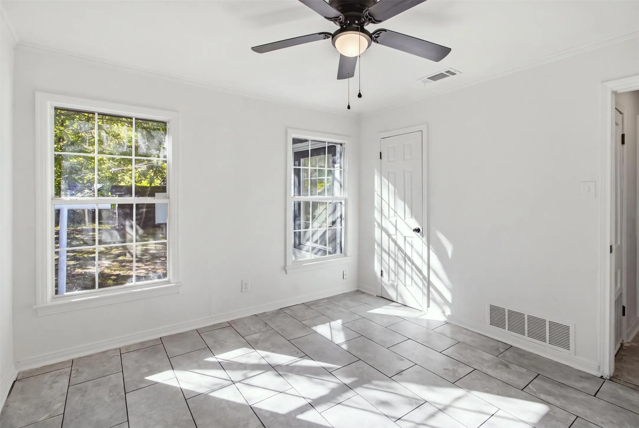 White painted interior with two grid-pattern windows, a ceiling fan with integrated lighting, and light-toned tile flooring