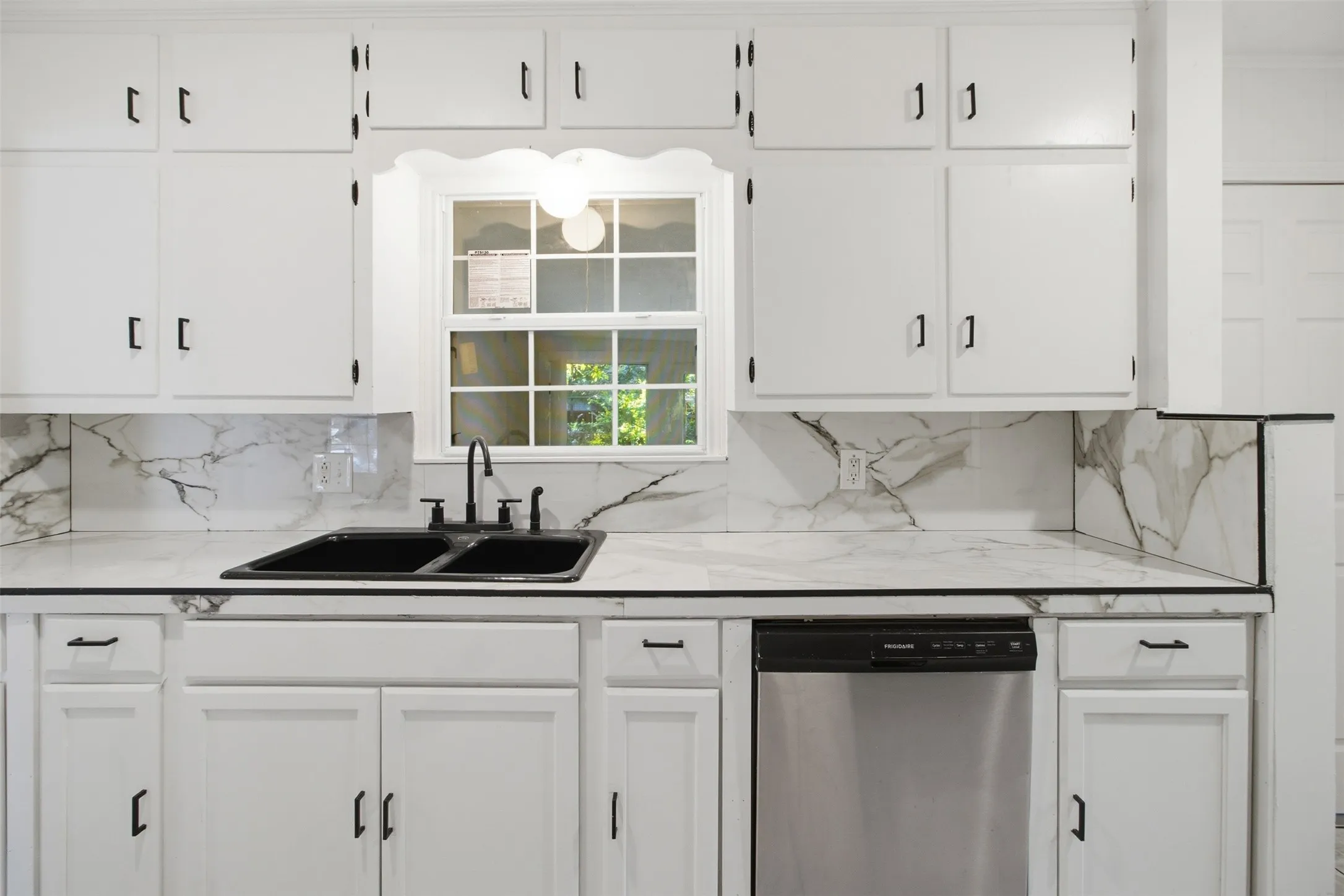 White cabinetry with black hardware, white countertops with veining, a black double basin sink with a black faucet, and a stainless steel dishwasher