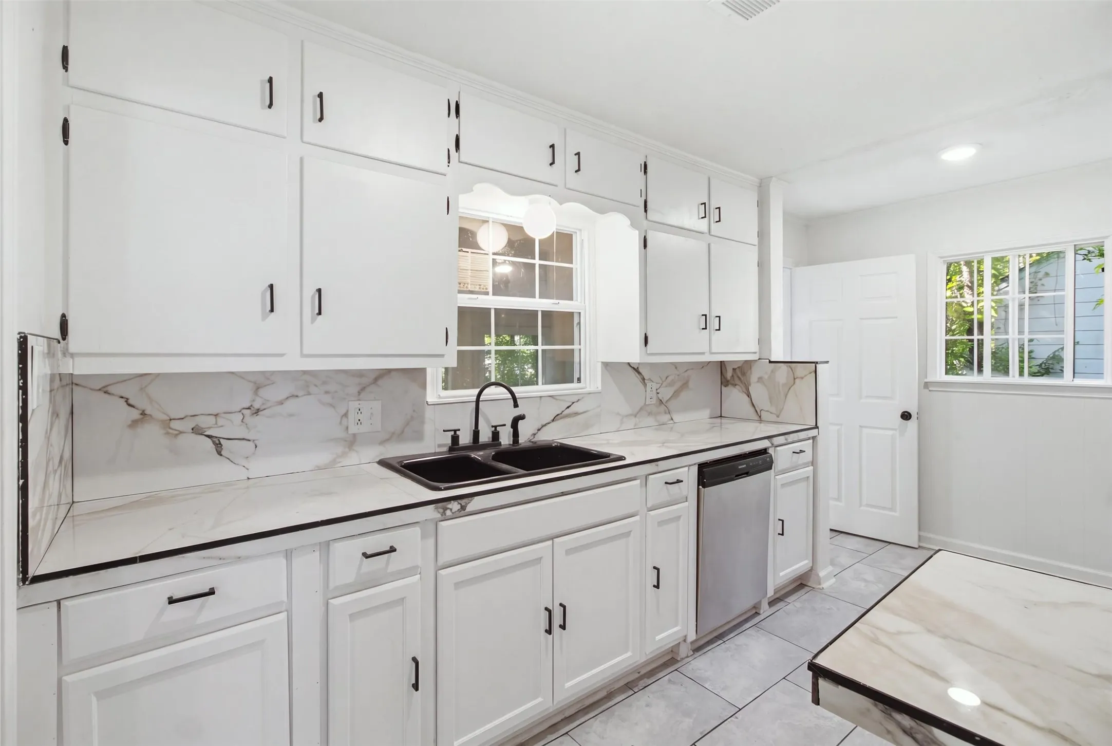 Kitchen featuring white cabinetry, a double basin sink, stainless steel dishwasher, and marble-look countertops with a matching backsplash