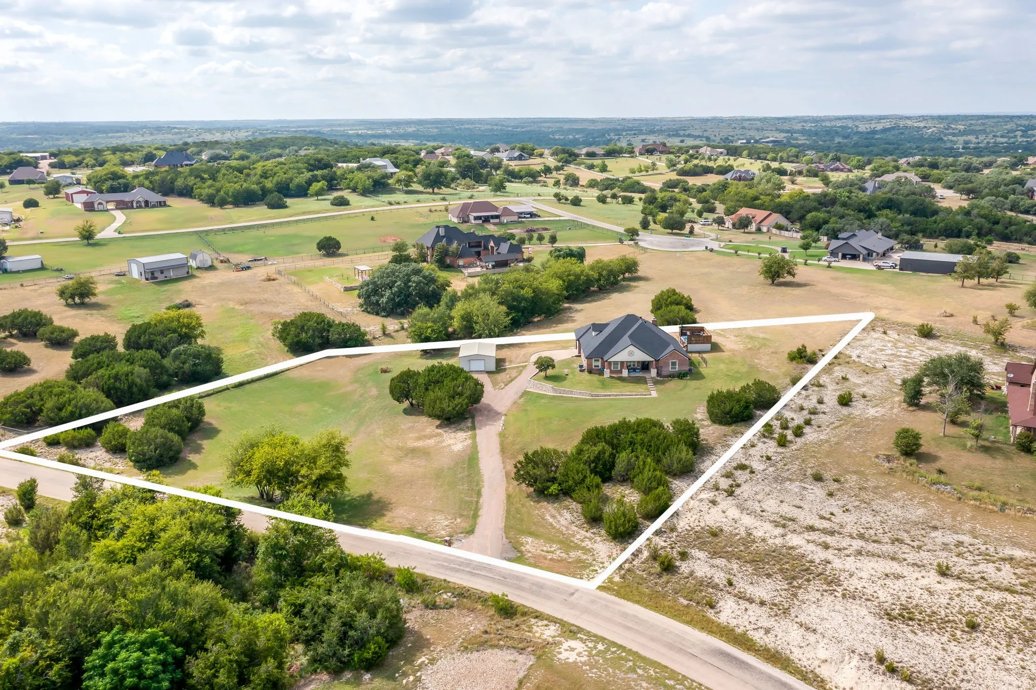 Spacious brick residence situated on expansive grounds with manicured lawn, mature shade trees, and a long driveway approach