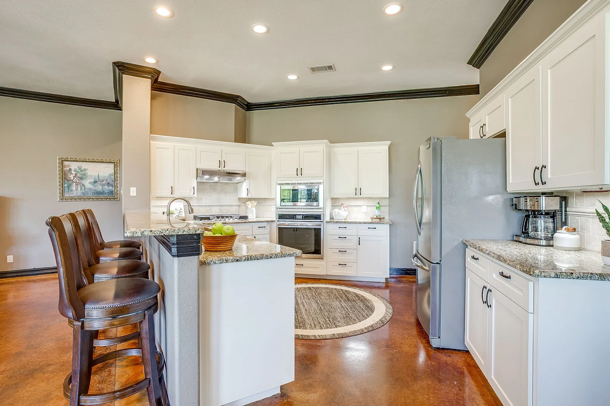 White shaker-style cabinetry, stainless steel appliances, granite countertops, recessed lighting, and a kitchen island with seating