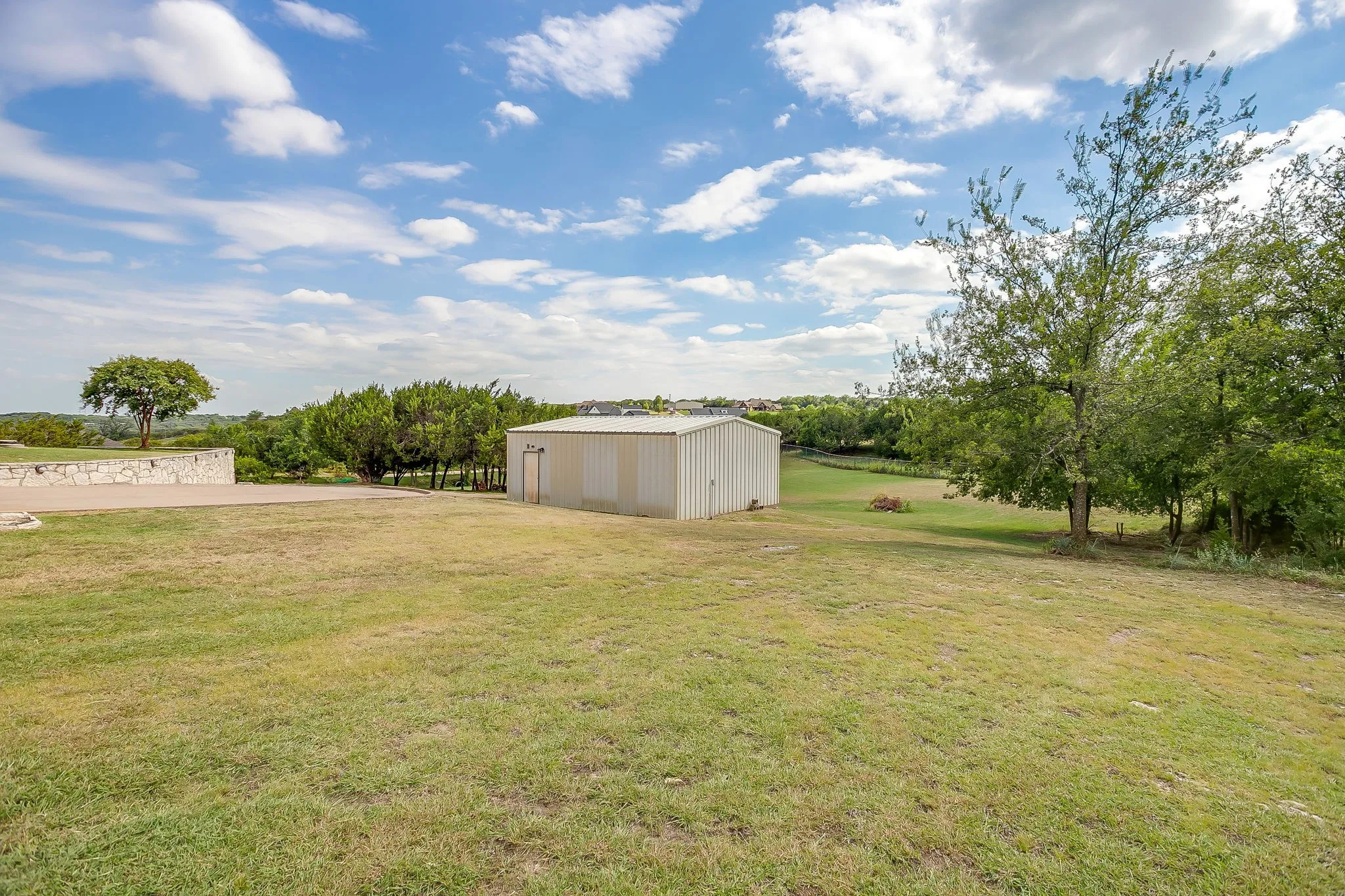 Expansive property featuring a brick residence, mature trees, and a gravel driveway
