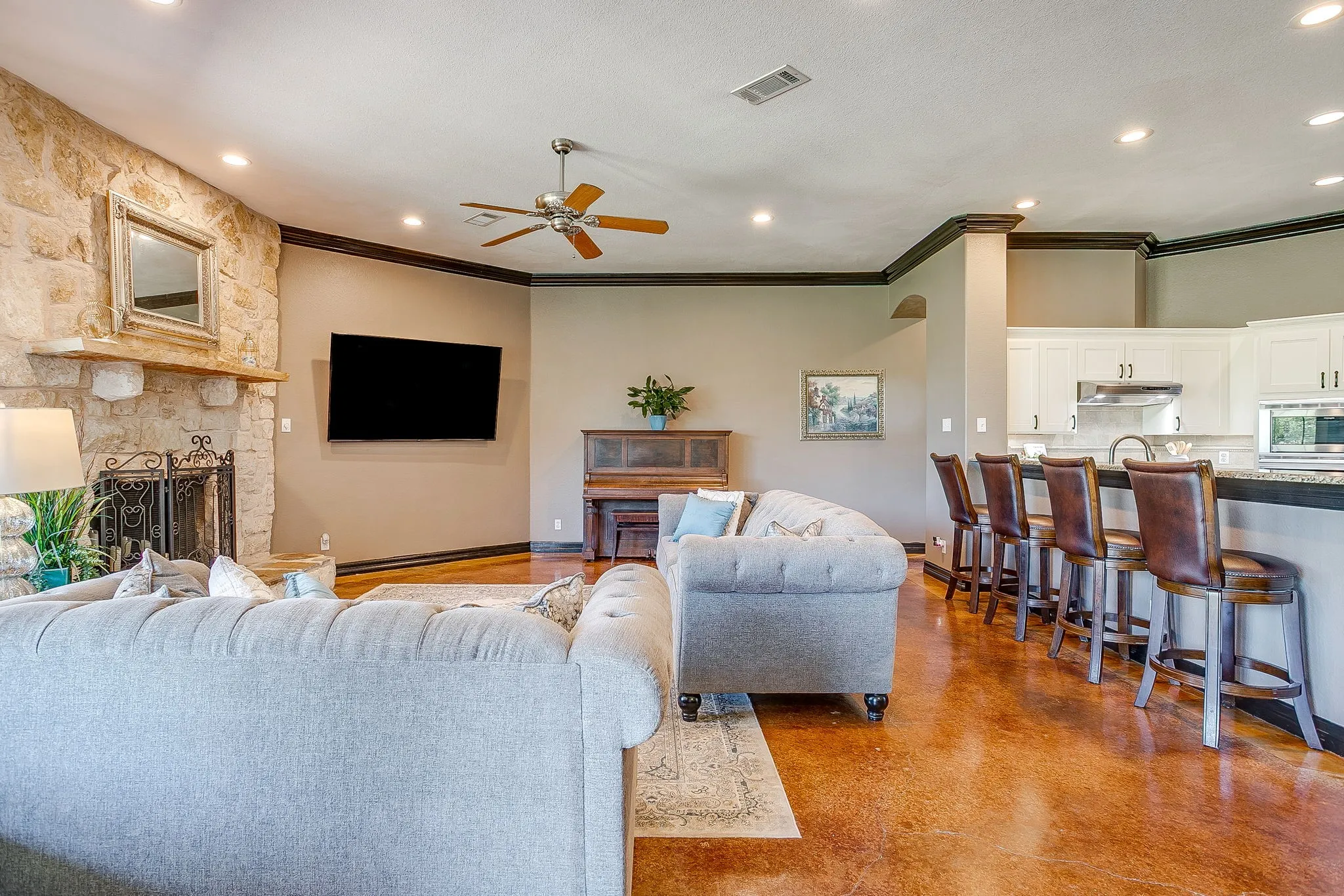 Stone accent wall with a fireplace and mantel, wood-finish flooring, recessed lighting, crown molding, and a kitchen bar with stone-finish countertops