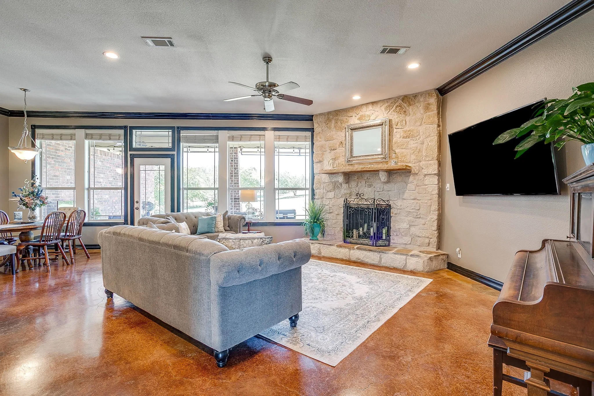 Stone fireplace with a wood mantle, ceiling fan with integrated lighting, recessed lighting, and a rear exterior door with glass panels