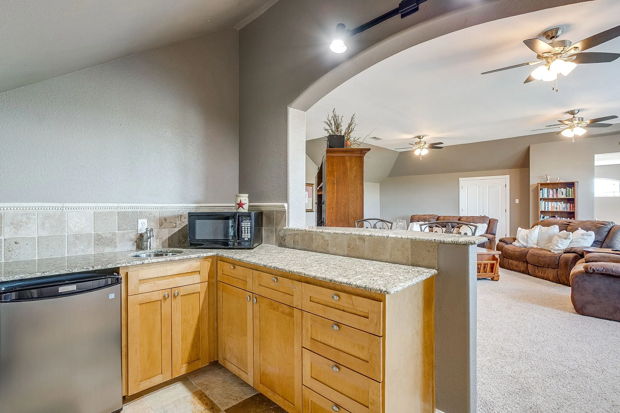 Upstairs built-in wet bar with wood cabinetry, granite countertops, and tile backsplash