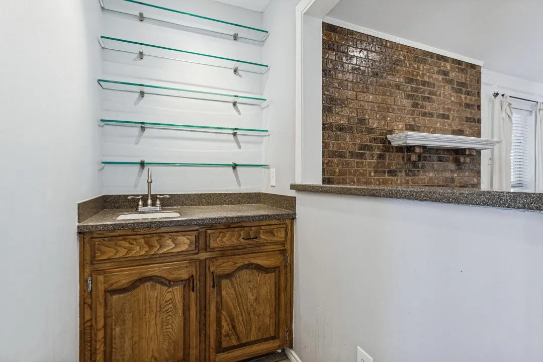 Built-in wet bar with wood cabinetry, granite-finish countertop, and a stainless steel sink
