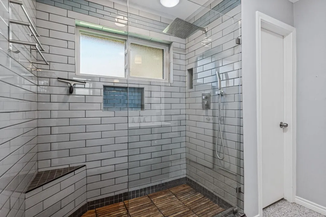 Glass-enclosed shower with subway tile surround, built-in bench, and wood-finish flooring