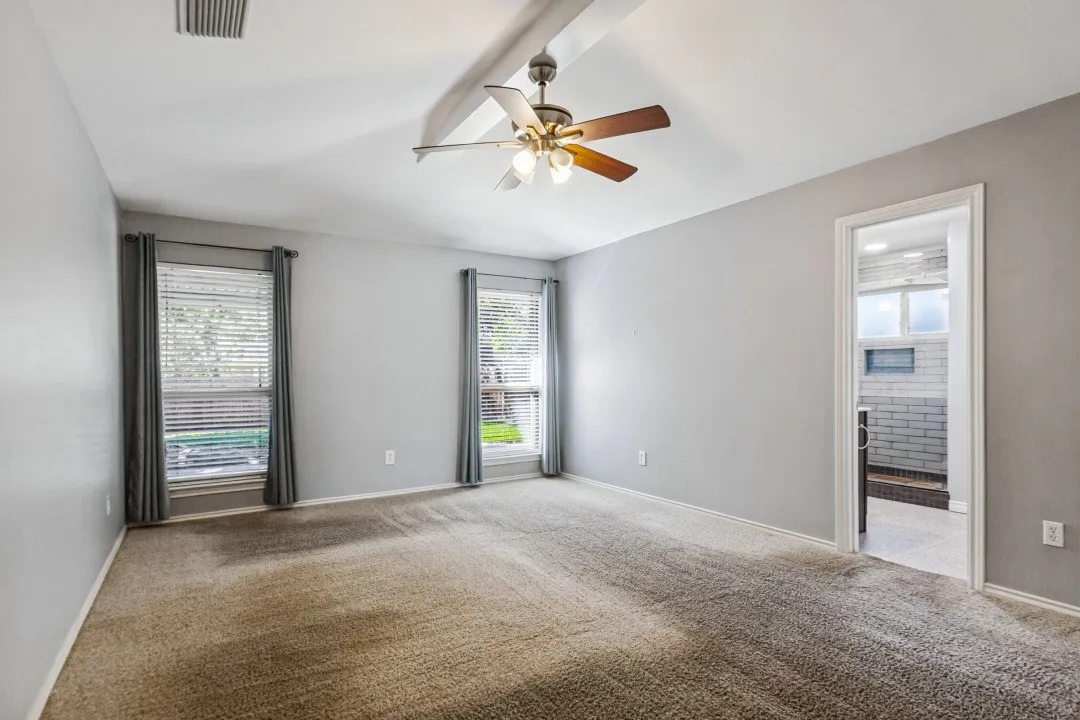 Vaulted ceiling with a ceiling fan, two windows, wall-to-wall carpeting, and an adjoining bathroom with subway tile