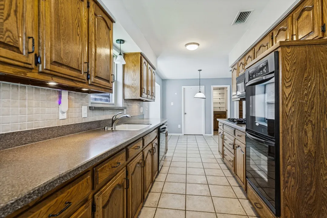 Galley kitchen featuring wood cabinetry, integrated double ovens, a built-in microwave, a tile backsplash, and tile flooring