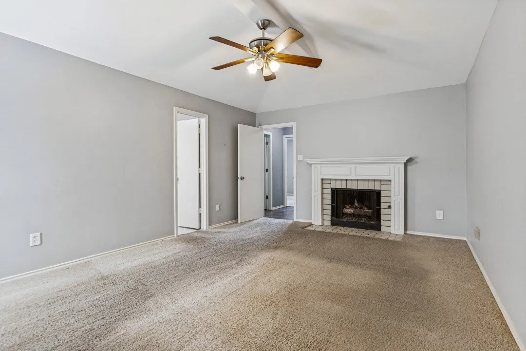 Vaulted ceiling with a ceiling fan, carpet flooring, and a fireplace featuring a white mantel and brick surround