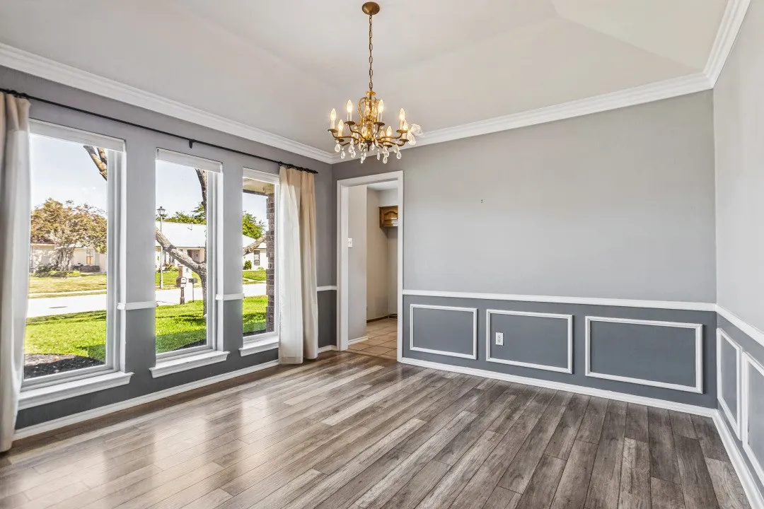 Wood-finish flooring, wainscoting, crown molding, and a decorative chandelier